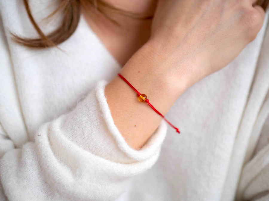 Pulsera ajustable de hilo rojo con ámbar báltico pulido color miel, ideal para equilibrio y bienestar