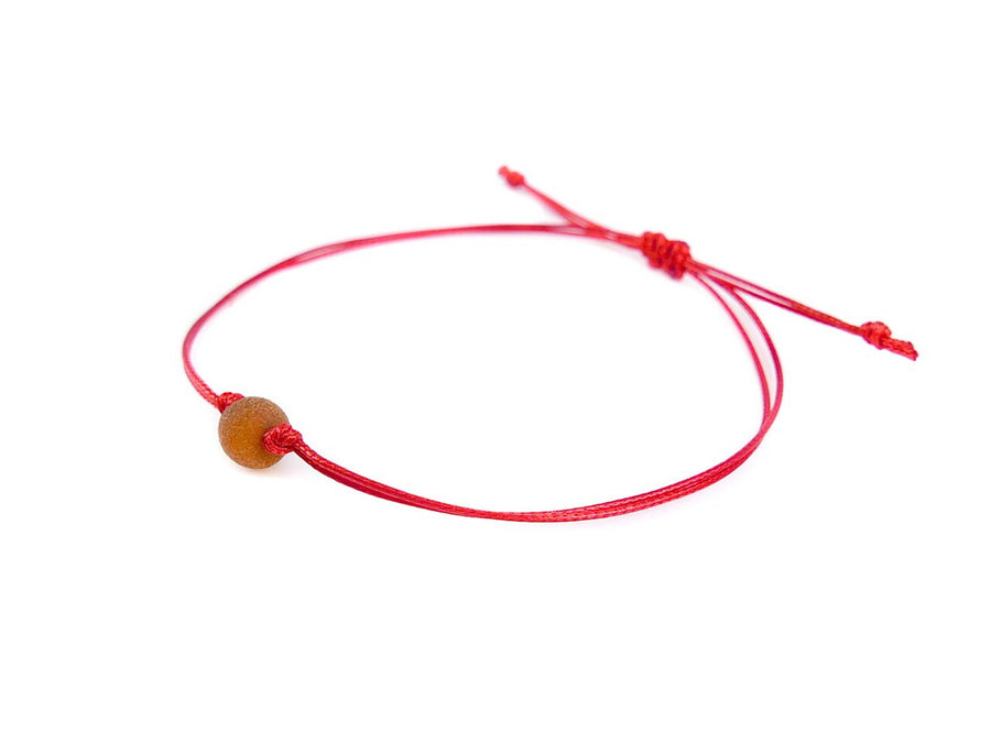 Pulsera artesanal de hilo rojo con ámbar sin pulir en tono coñac, ideal para bebés y adultos